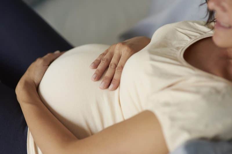 woman holding her pregnant belly comfortably on couch