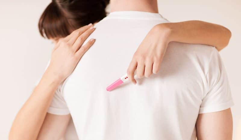 close up of woman with pregnancy test hugging man